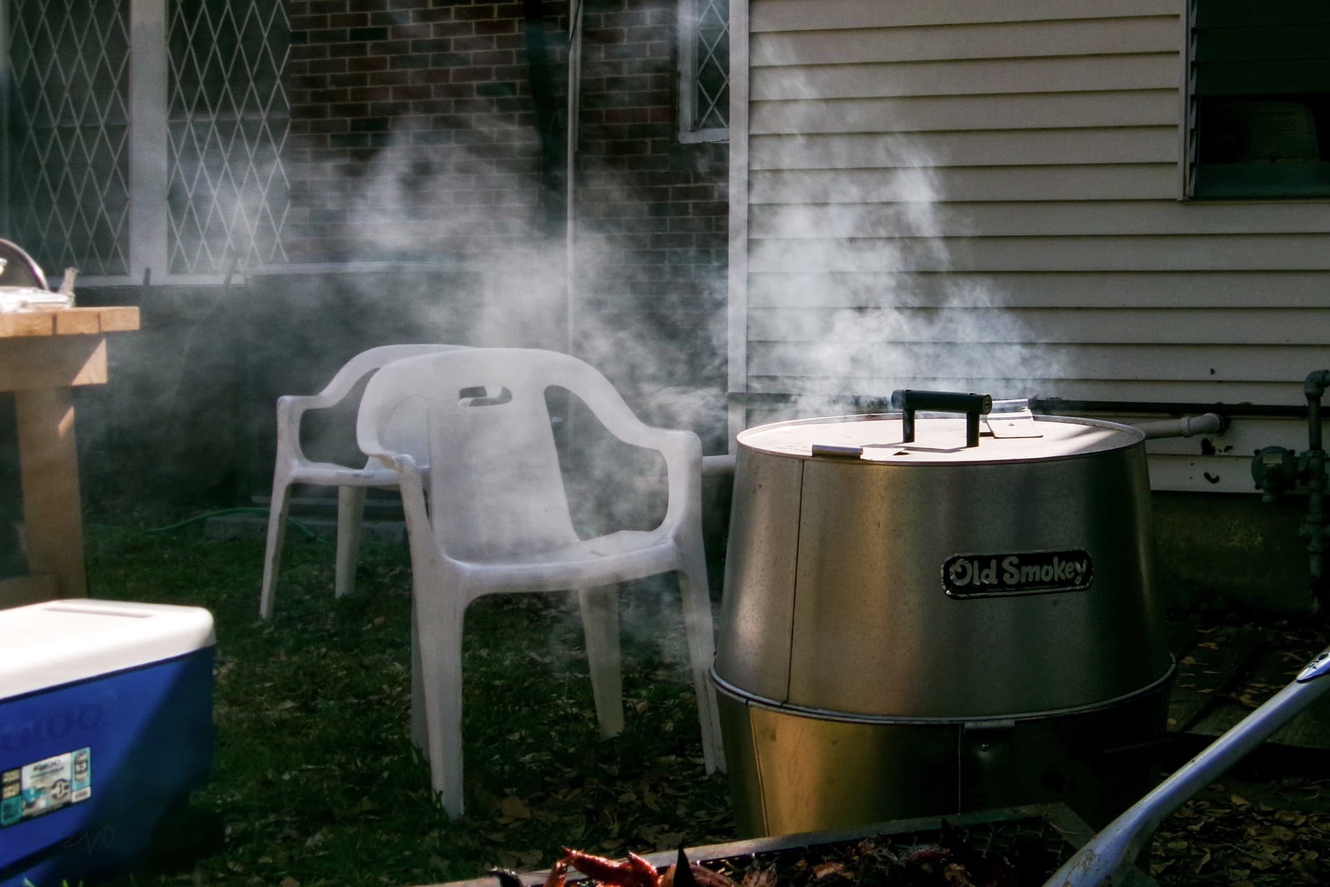 Smoke rising from a charcoal drum smoker in a backyard on a sunny afternoon